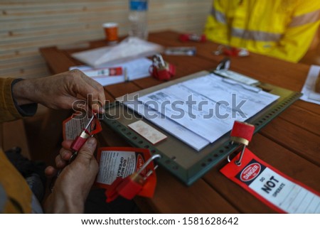 Close up top view of construction worker hand placing personal red danger lock which is attached together with danger tag into isolation safety control permit lock box prior to starting each shift  Royalty-Free Stock Photo #1581628642