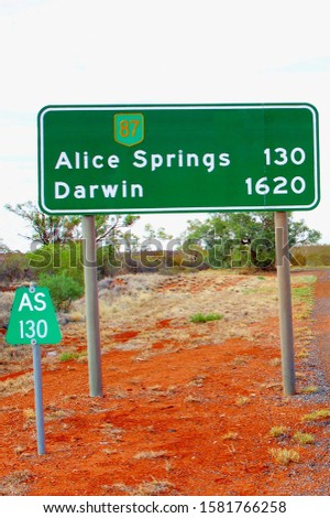 Traffic signage signs to Alice Springs and long distances to Darwin in north direction, desert landscape in Northern Territory, Australia