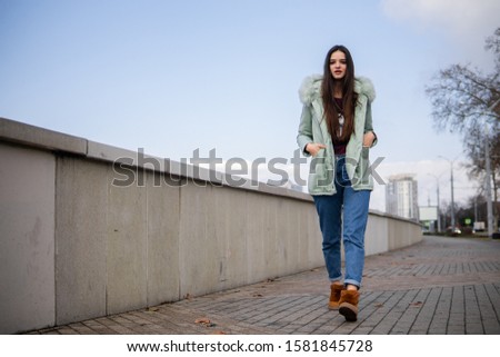 Girl in the city in winter. Girl on a walk in the city by the river. Cold weather, a girl in a warm jacket. Blue sky/