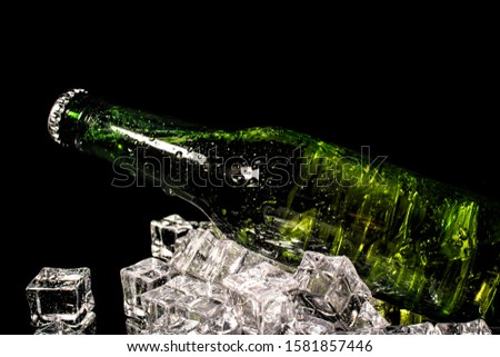 Cold beer in a green bottle, with water drops and ice cubes, with dark background