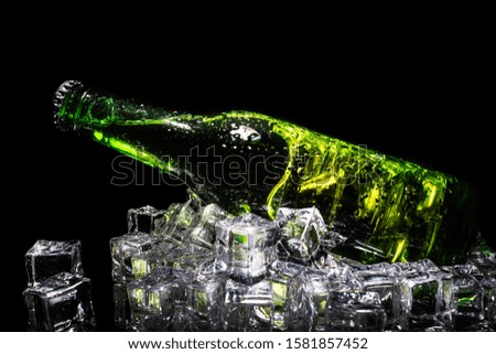 Cold beer in a green bottle, with water drops and ice cubes, with dark background