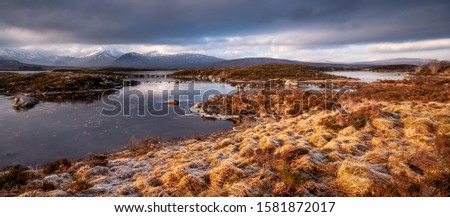 Winter ice coats Lochan na h-Achlaise lake on the vast peat bog moorland of Rannoch Moor, with the snow-capped Black Mountains in the distance. Royalty-Free Stock Photo #1581872017