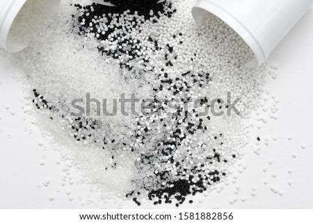Glass with transparent, black and white termoplastic elastomer granules on a white background Royalty-Free Stock Photo #1581882856