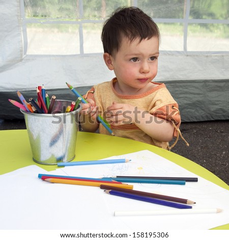 Portrait of a small child, boy or girl, drawing picture and playing with crayons.