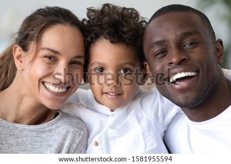 Head shot portrait close up smiling African American mother, father and son with healthy white smiles, happy family posing for photo, looking at camera, cute little child embracing parents Royalty-Free Stock Photo #1581955594
