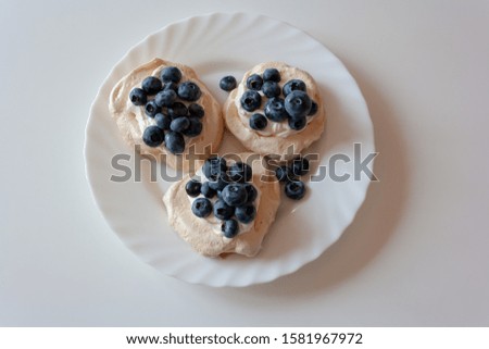 Pavlov cakes with cream and fresh blueberries on a white plate