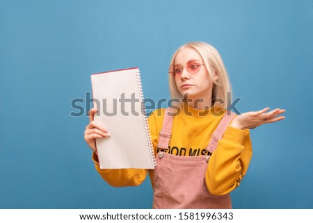 Portrait of a funny teen girl with a puzzled face reading a notebook, focused looking at the text isolated on the background. Funny girl student prepares a homework, confused reading notebook.