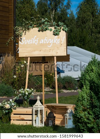 A sign at the entrance of the wedding hall saying "Welcome" decorated with eucalyptus and candles