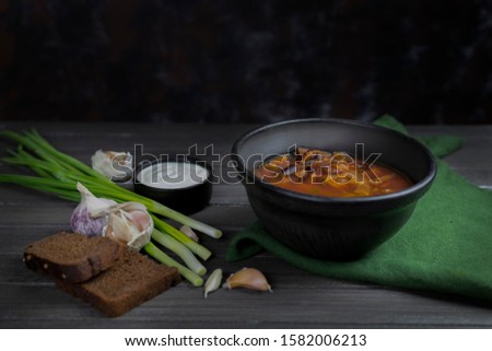 red borsch, a traditional national dish of Ukrainian cuisine.in the stock photo, the borsch is served in a black pottery with sour cream, green onions and garlic on a dark wooden background using gren