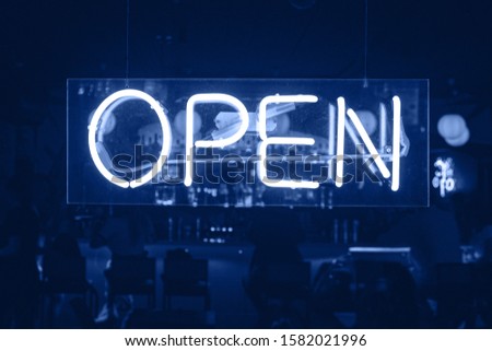 Neon Sign Glowing At Night Behind Glass: Open. Nightlife and party concept. Friday rest at bar. Toned in Classic Blue Color - Trend Color of New Year 2020.