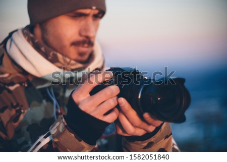 Photographer with camera at sunset during frozen winter evening in the mountains