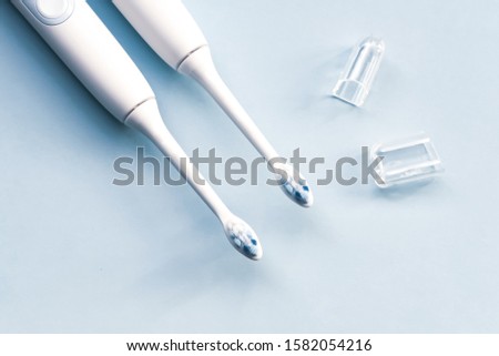 White electric toothbrush, brush heads, case on pastel blue background.