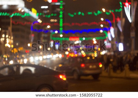 Blurred picture of urban illumination in honor of the winter holidays. View of the road, car lights and multi-colored Christmas garlands out of focus.