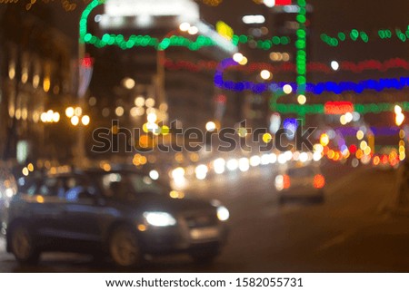 Blurred picture of urban illumination in honor of the winter holidays. View of the road, car lights and multi-colored Christmas garlands out of focus.