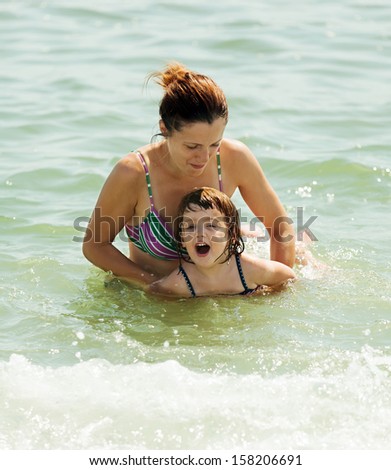 mother teaching daughter to swim in sea wave