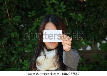 The Asian woman holds the white blank paper for text or message in hand