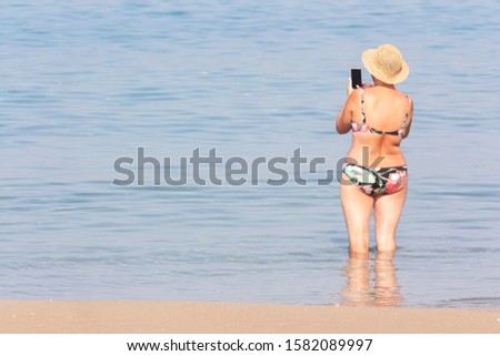 A woman in a swimsuit takes pictures of the sea on a smartphone