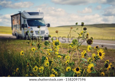  24’ class c RV motorhome parked on side of two-lane highway slightly out of focus in the background with roadside daisies in focus in the foreground.                            Royalty-Free Stock Photo #1582097596