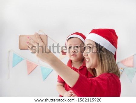 Happy asian woman and her son in Santa hat take photo by smartphone.