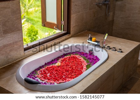 A romantic bath with various flowers making a heart shape with window open