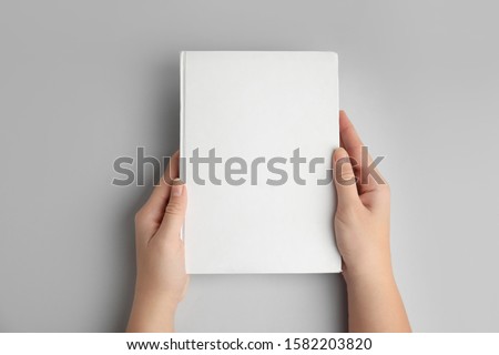 Woman holding book with blank cover on grey background, top view Royalty-Free Stock Photo #1582203820