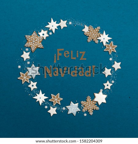 Cut out paper letters spelling "Feliz Navidad" - "Merry Christmas" wishes in Spanish. Christmas wreath with ginger cookies shaped like stars and snowflakes.