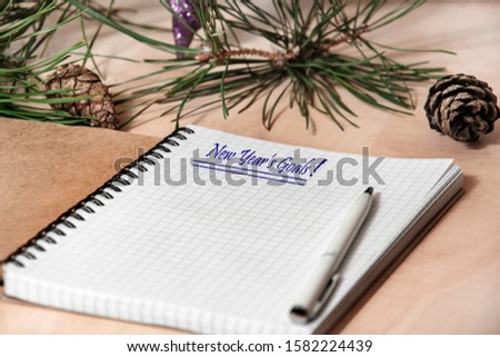 Opened notepad on a wooden desktop. the inscription on the first page: "New Year's goals." on a table nearby lies a pine branch.
