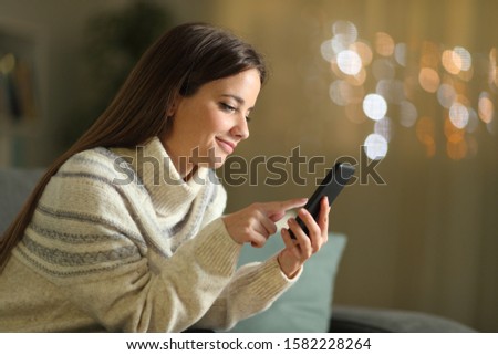 Side view portrait of a woman using mobile phone sitting on a couch in the night at home in winter