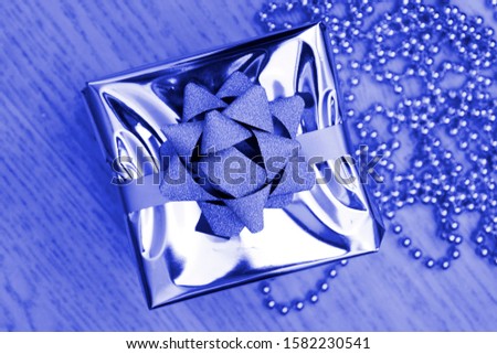 Gift box with bow in silver wrap in blue light. New Year, Christmas concept. Pantone color 2020 - classic blue