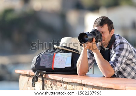 Tourist taking photos with a digital camera on vacation standing in a balcony outdoors in a rural town