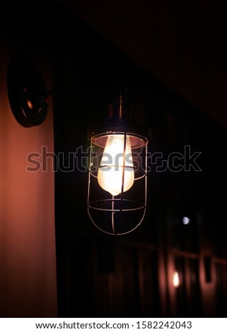 vintage hanging electric lamp in old hotel corridor , in black night with little blurred reflect light from the door behind