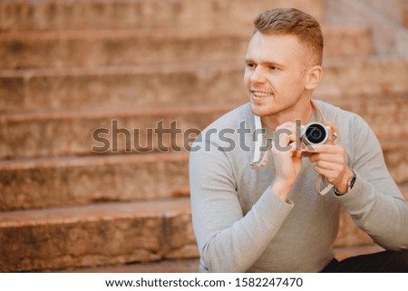 Portrait happy male traveler photographer holding camera in hands sitting on steps in italy, blurred background.
