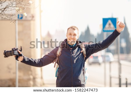 Portrait happy male traveler photographer holding camera in hands, blurred background.