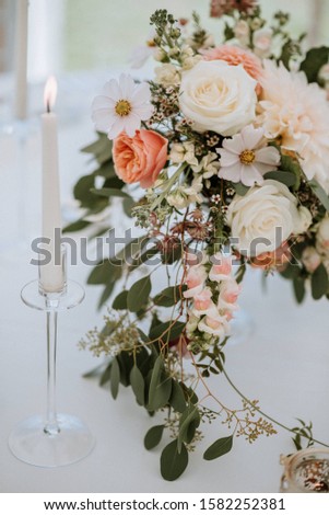 A vertical closeup shot of a flower bouquet and a taper candle on a white table