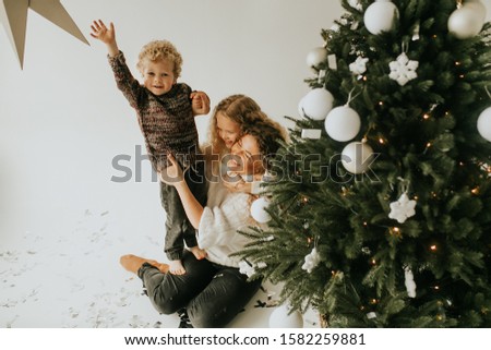 mother with children plays near the Christmas tree and decorates her