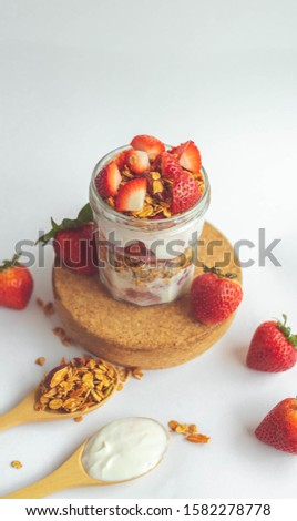 a jar with tasty parfaits made of healthy granola, strawberries and Greek yogurt on white background. Shot at angle.