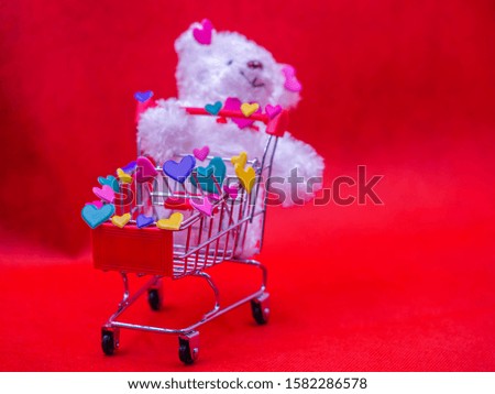 Closeup of heart shape stickers on shopping cart with blurry white dog doll on vivid, vibrant red background for love, valentine, shopping, birthday, business, greeting card concept.