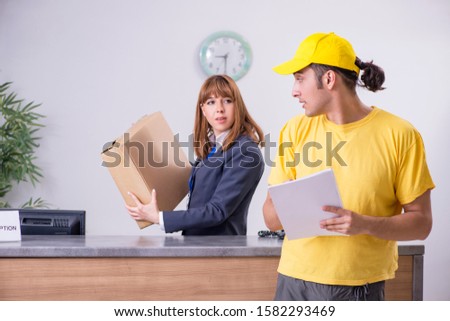 Young male courier delivering box to hotel's reception