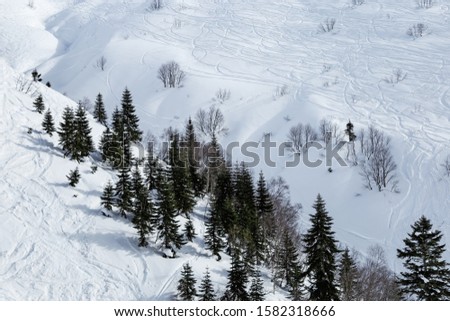 Ski tracks on white snow in winter mountains. Mountain slope in Rosa Khutor ski resort in Russia. Holidays and active rest in mountains. Wintertime and blue clouds on sky. 