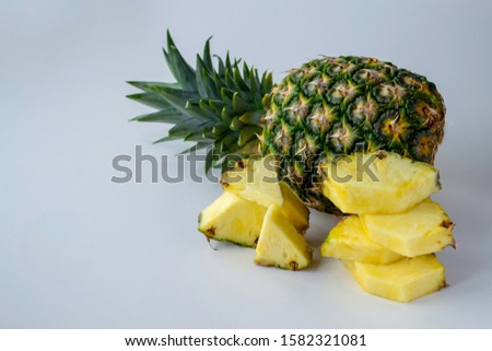 Pineapple lies on a light gray uniform surface. And the sliced ​​pieces lie next to the column. Place for your text.