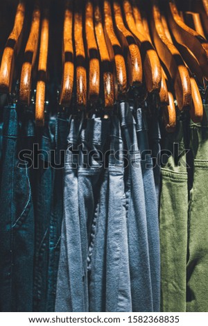 picture of jeans on wooden hangers in a shop under a warm yellow spotlight. moodie feeling.