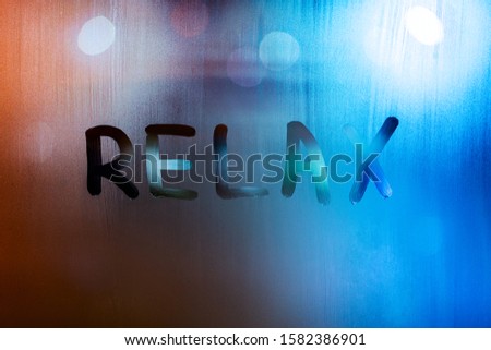 the word relax written by finger on wet glass with blurred lights in background.