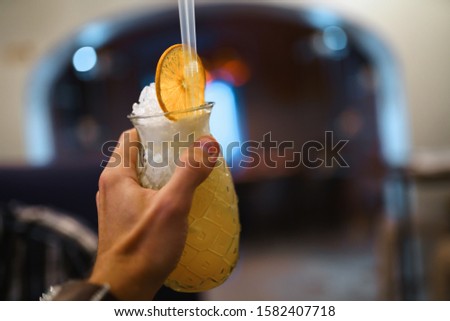Man hand holding an orange summer cocktail in a medieval restaurant hall - Blurry  bokeh