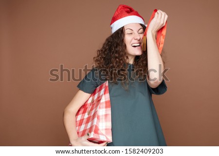 Funny happy pregnant overjoyed female feels hungry, ready to bite fresh made cookies which she prepared as gifts for Christmas party, holding checkered box, isolated on brown studio wall background.