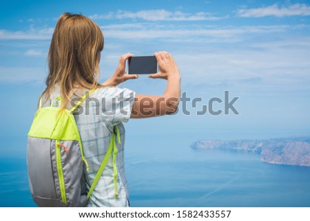 Girl hiker take a photo of distant cape in a sea with new smartphone.