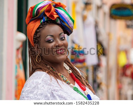 Happy Brazilian woman of African descent dressed in traditional Baiana costumes in the Historic Center of Salvador da Bahia, Brazil. Royalty-Free Stock Photo #1582435228