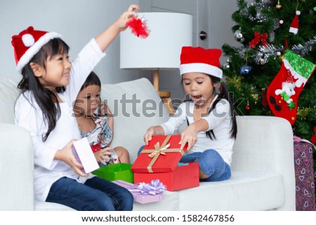 Selective focus lovely girl opening red present box and two childrens sitting on couch and opening christmas present with exciting and happiness, beautiful christmas tree decorated nearly