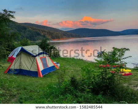 A beautiful shot of a tent on the grass by a lake with hills in the background at sunset