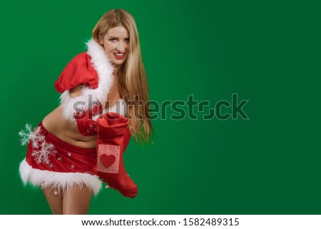 Beautiful emotional young girl with long hair dressed as Santa Claus with a Christmas sock for gifts in her hands posing on a green chrome background