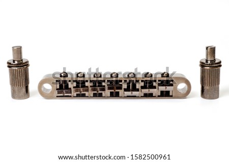Metallic guitar bridge, suitable for electric and acoustic guitars, disassembled, closeup shot on a white background.